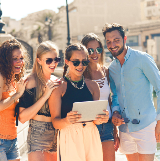 Young adult friend group looking at tablet and smiling while outdoors